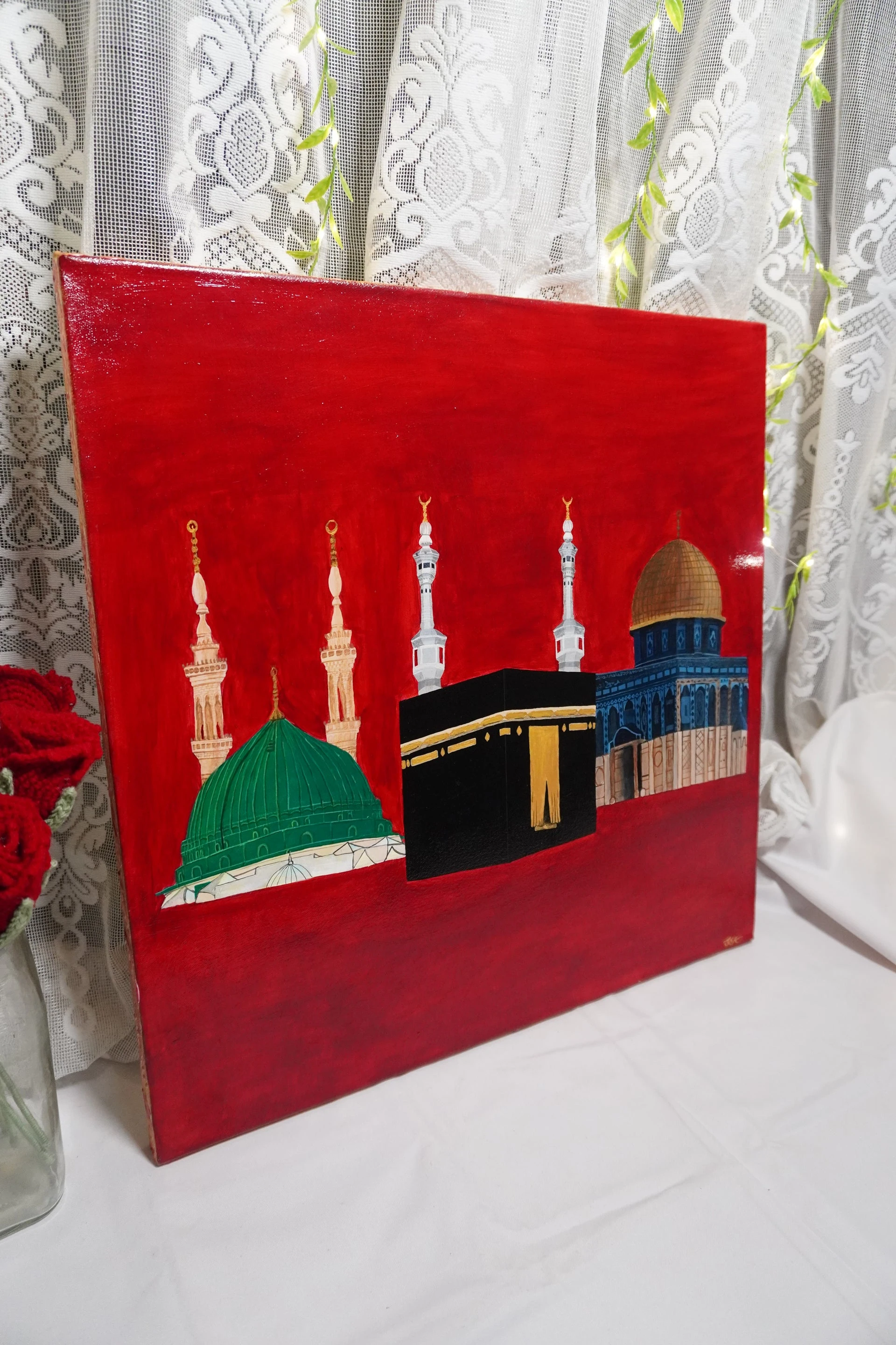 Al-Wahda photographed upright in the studio, with its red background and three painted sacred sites visible against a lace curtain.