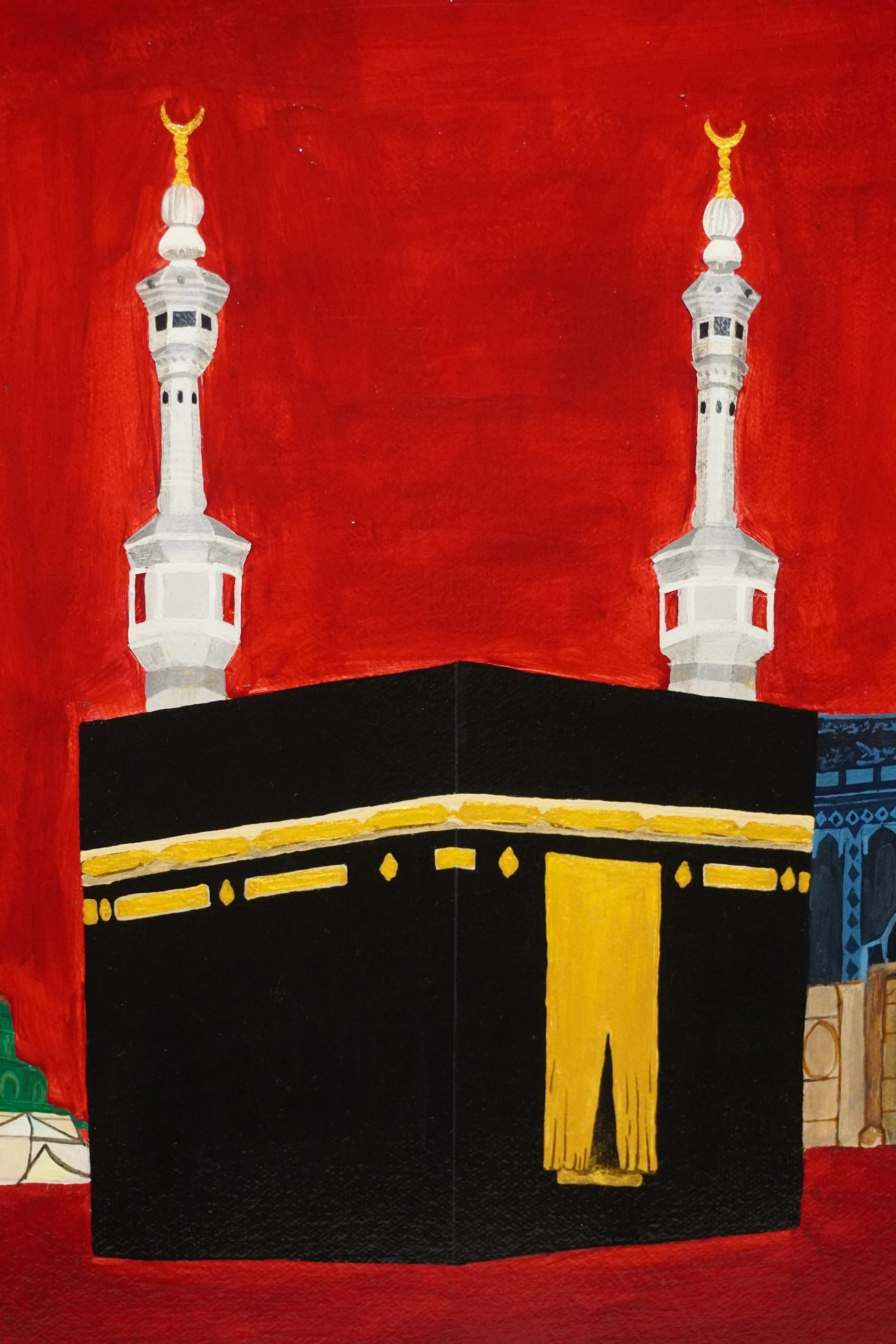 A close view of the black-and-gold Kaaba and two white minarets in Al-Wahda, showing the painted marks against the red background.